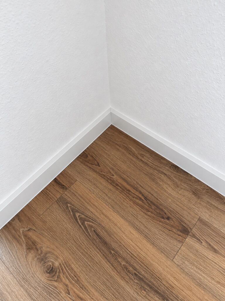 Weiße Sockelleisten an einer Innenecke mit Boden in brauner Holzoptik