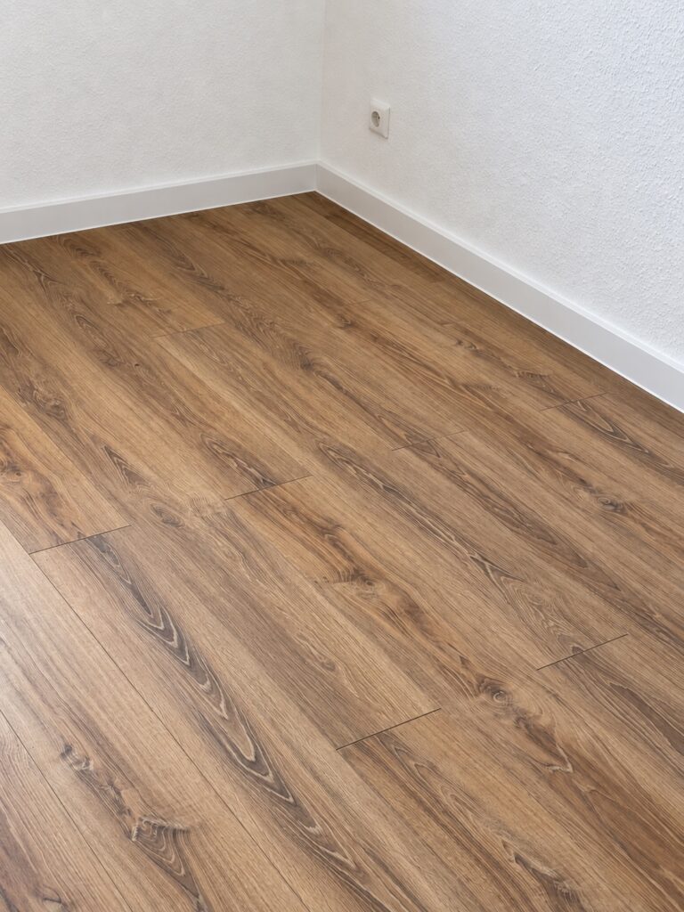 Raumecke mit weißen Wänden, Sockelleisten und Boden in Holzoptik