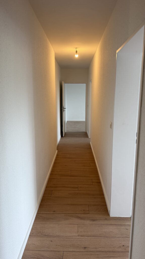 Wand- und Bodenflächen in einem schmalen Flur mit mehreren Türöffnungen.