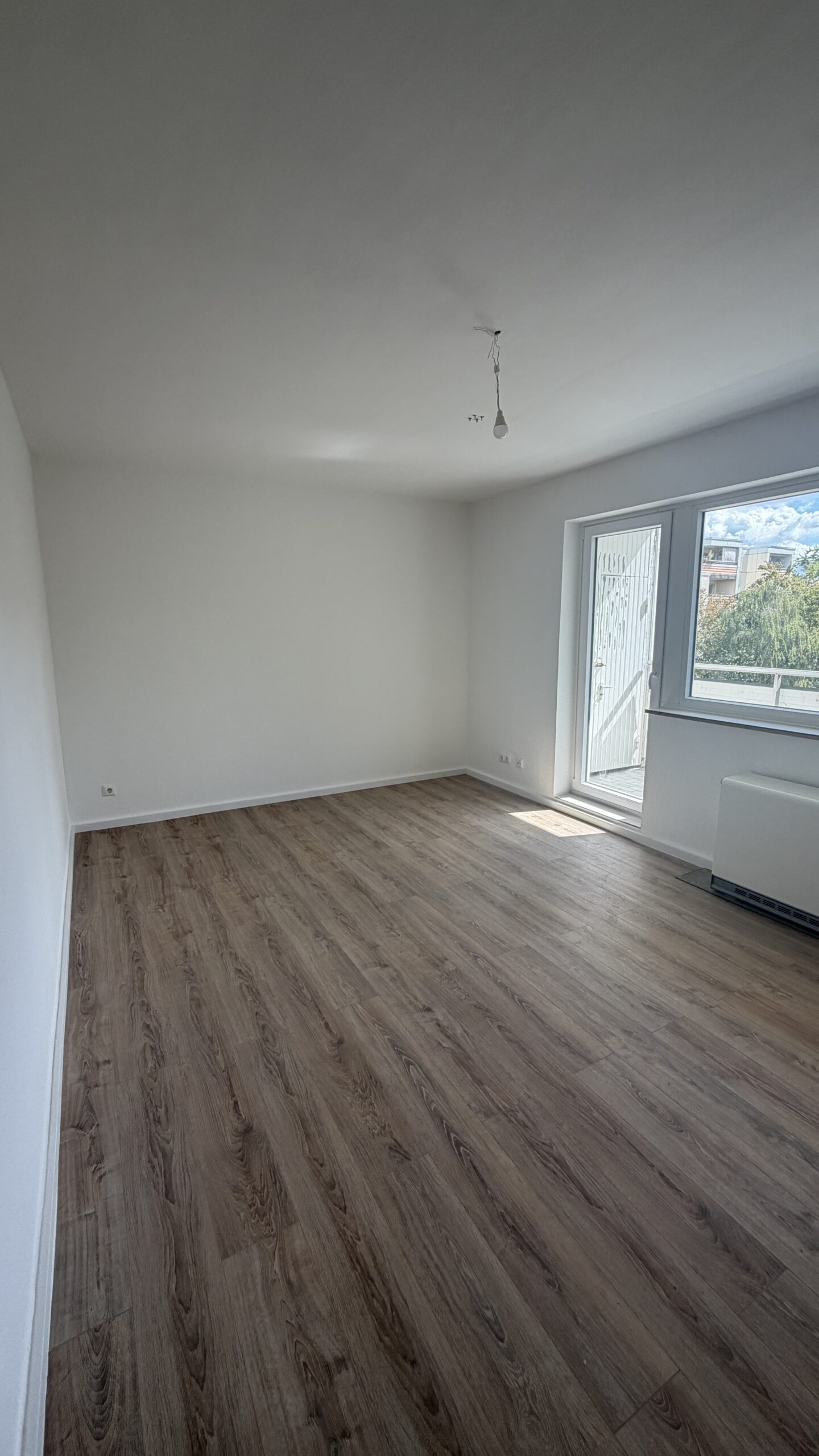 Weiße Wandflächen, Boden in Holzoptik und helle Sockelleisten in einem Wohnraum mit Balkonzugang.