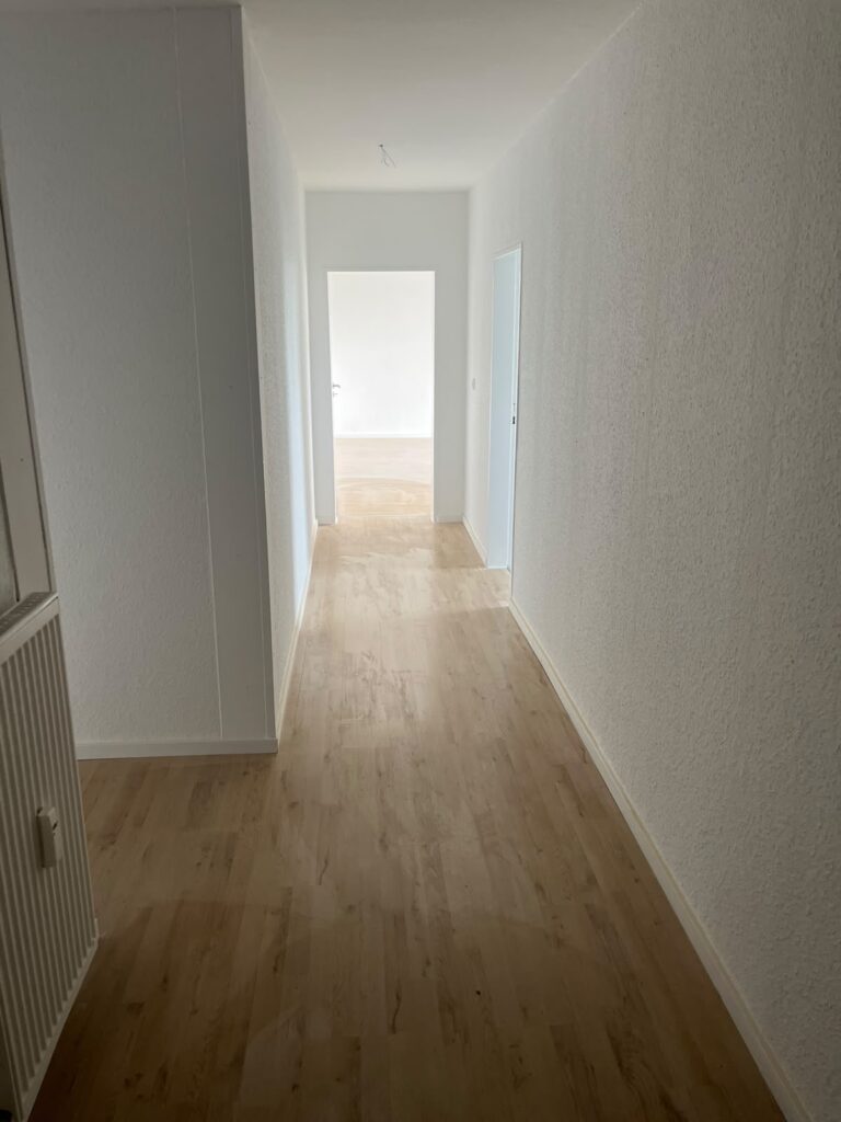 Weiß gestaltete Wände und Boden in Holzoptik entlang des Wohnungsflurs.