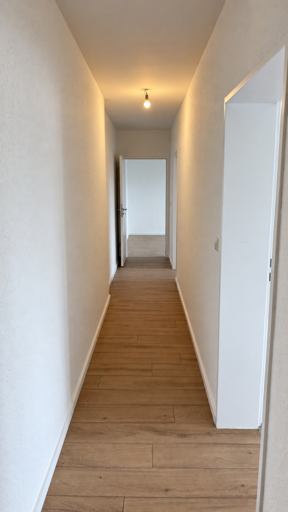 Schmaler Flur mit weißen Wänden, weißen Türrahmen und Boden in Holzoptik